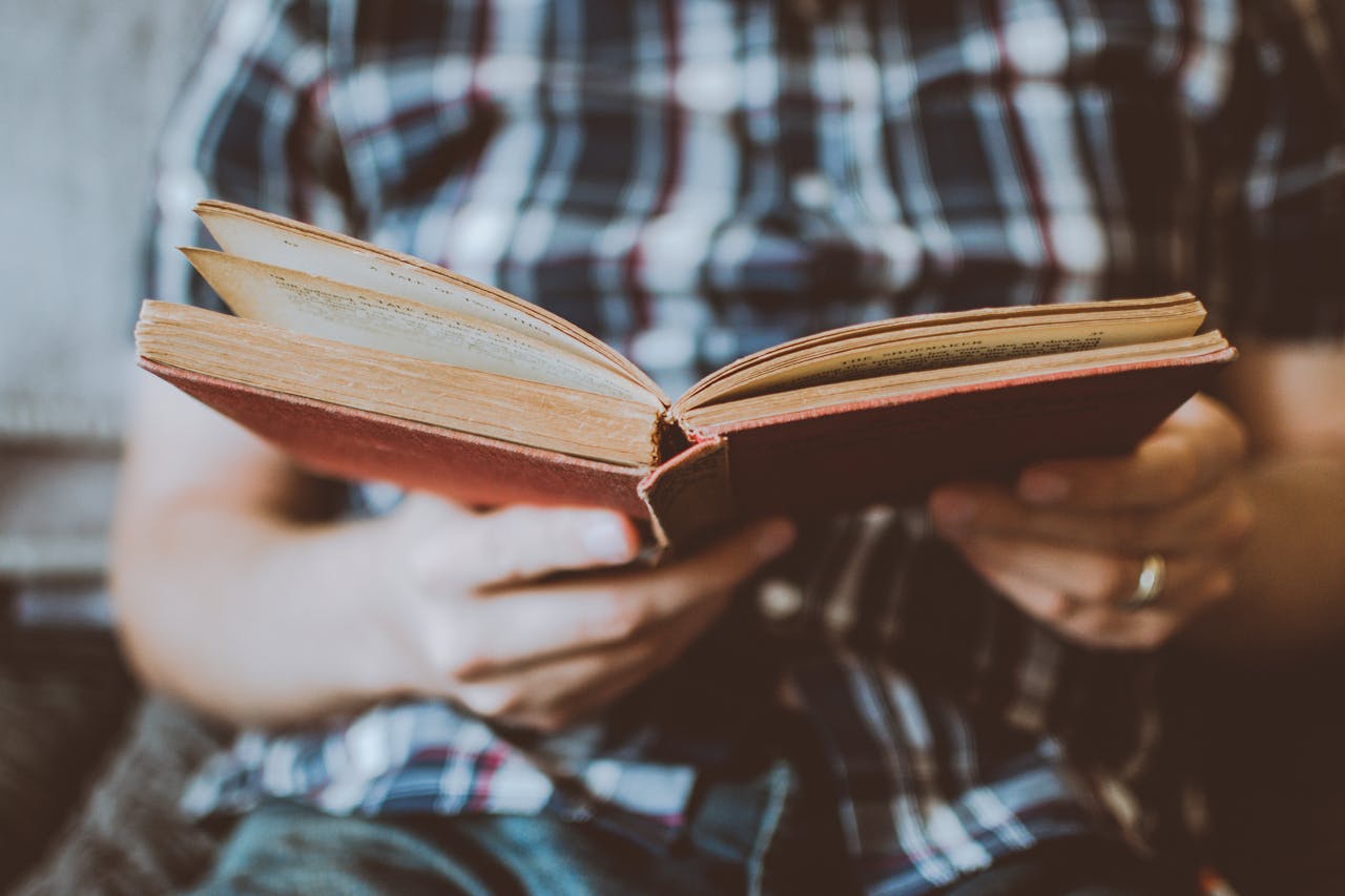 Close-up of hands holding and reading an antique book indoors, symbolizing knowledge and learning.