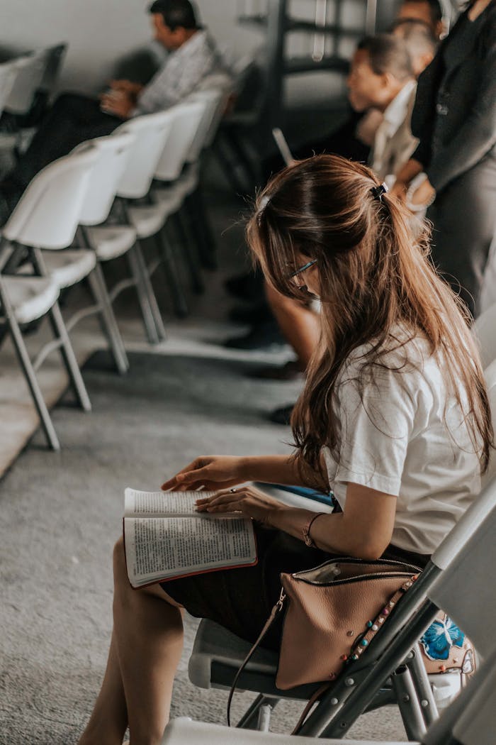 Focused woman reading a book in an academic setting with others in the background.